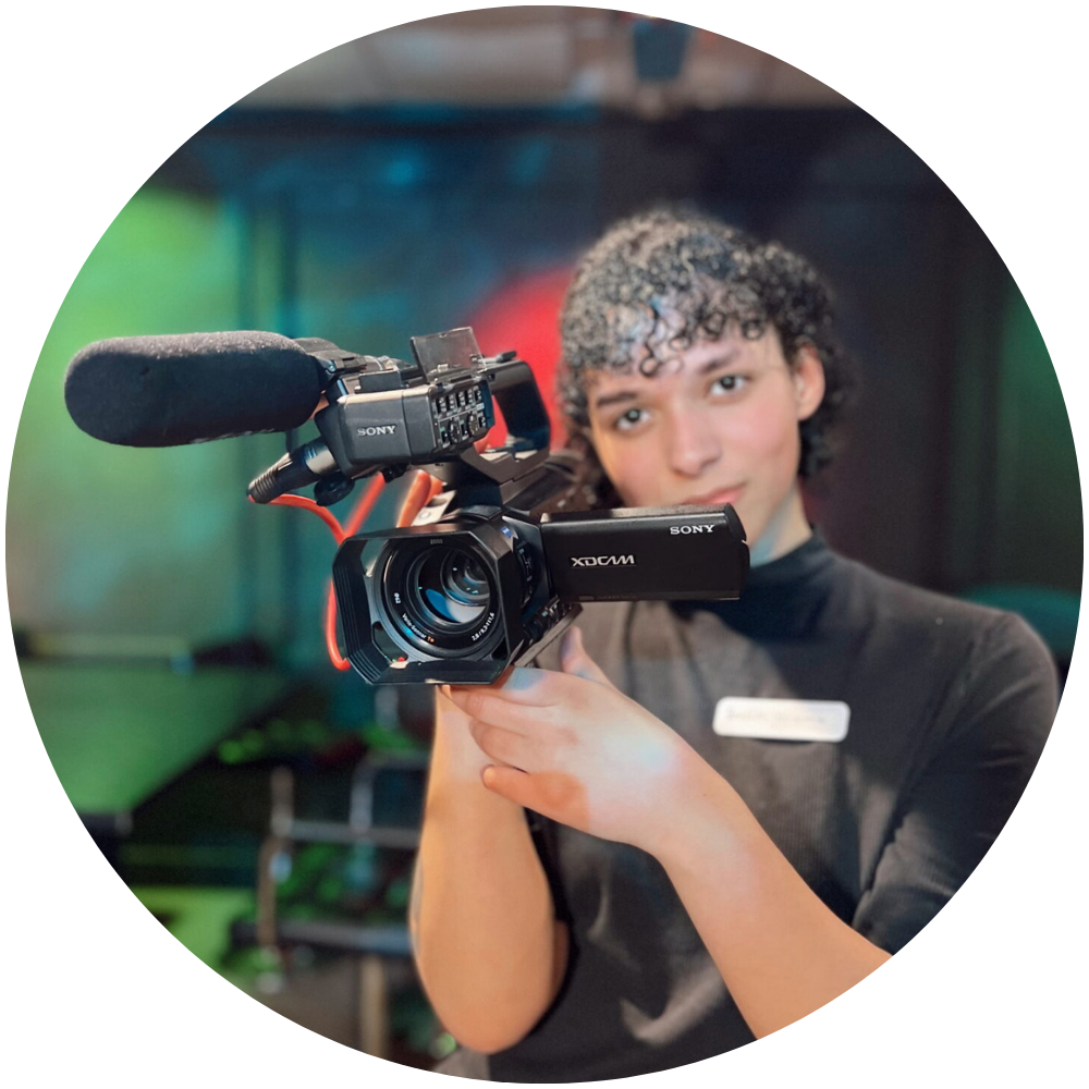Photograph of Ari Santos posing with a camera in the GNAT studio.